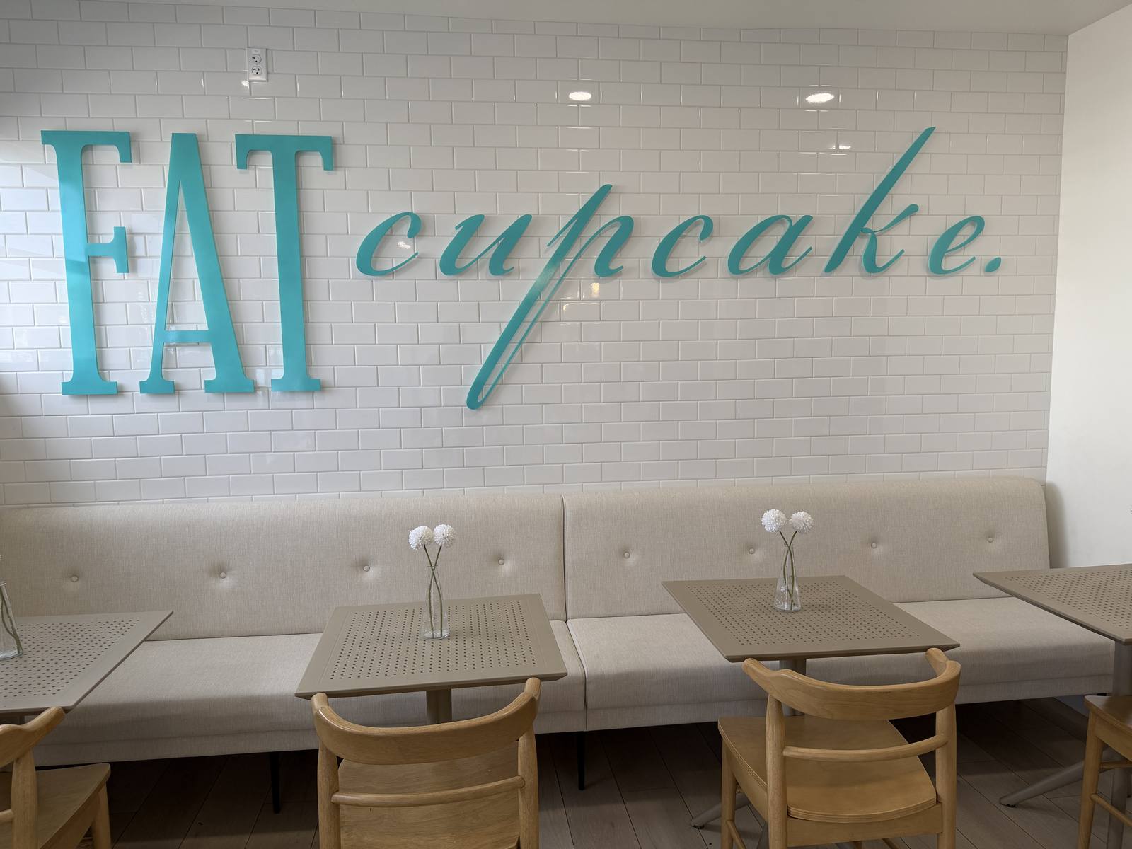 Fat Cupcake interior on Woodstock: teal logo on subway tile, cream banquette.